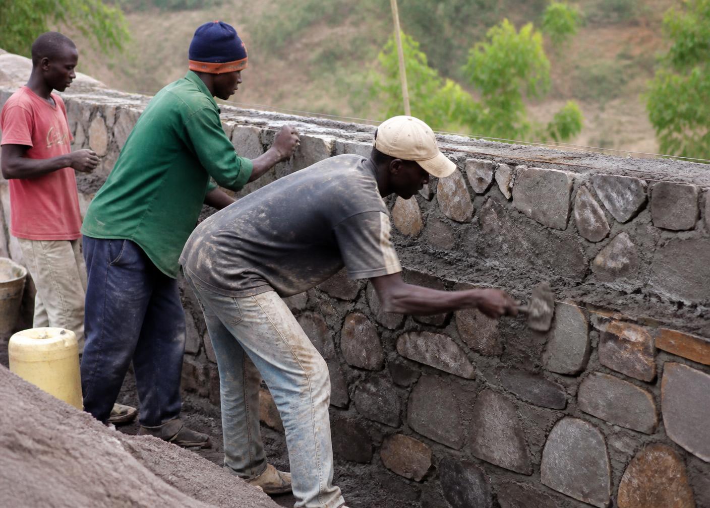 Kenyan builders hand-finishing a natural stone wall on site